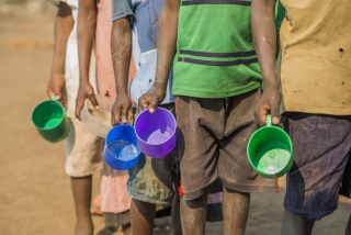 Children from Malawi waiting in line with their porridge mugs to receive Mary's Meals at school. 